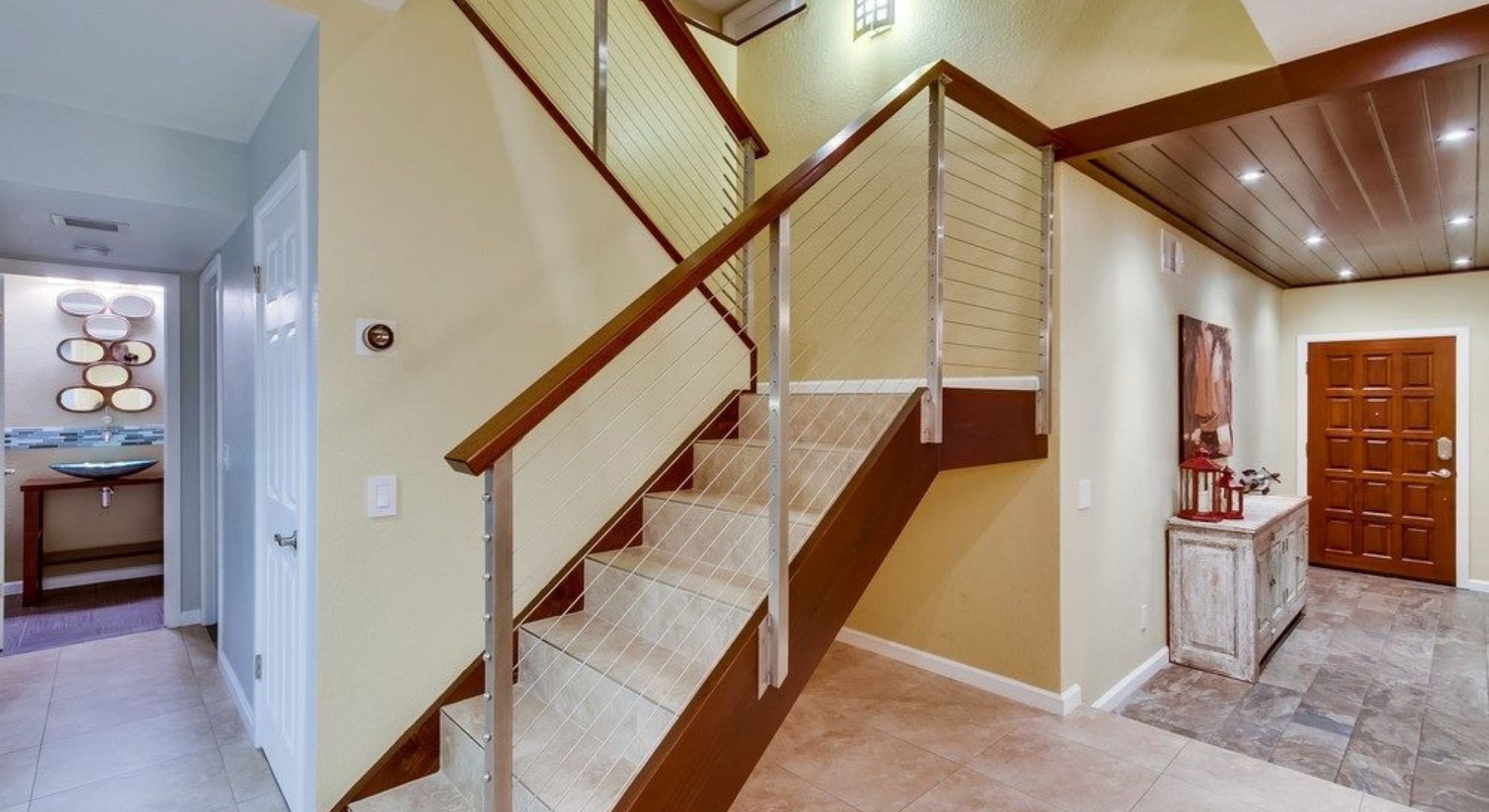 Modern interior staircase with stainless steel cable railing and wood handrail in a bright, open-concept luxury home.