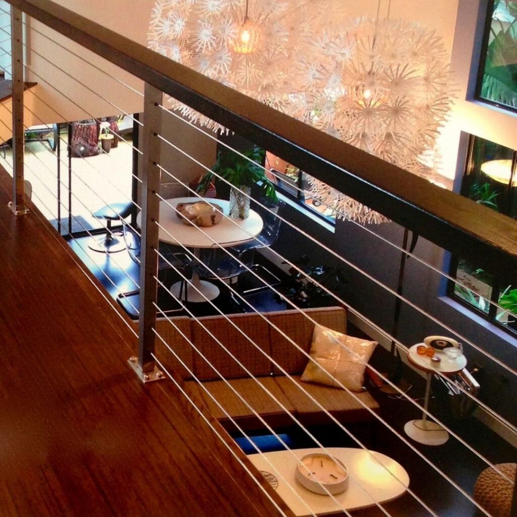 Interior balcony railing combining stainless steel cables with a warm wood top rail for a transitional design.