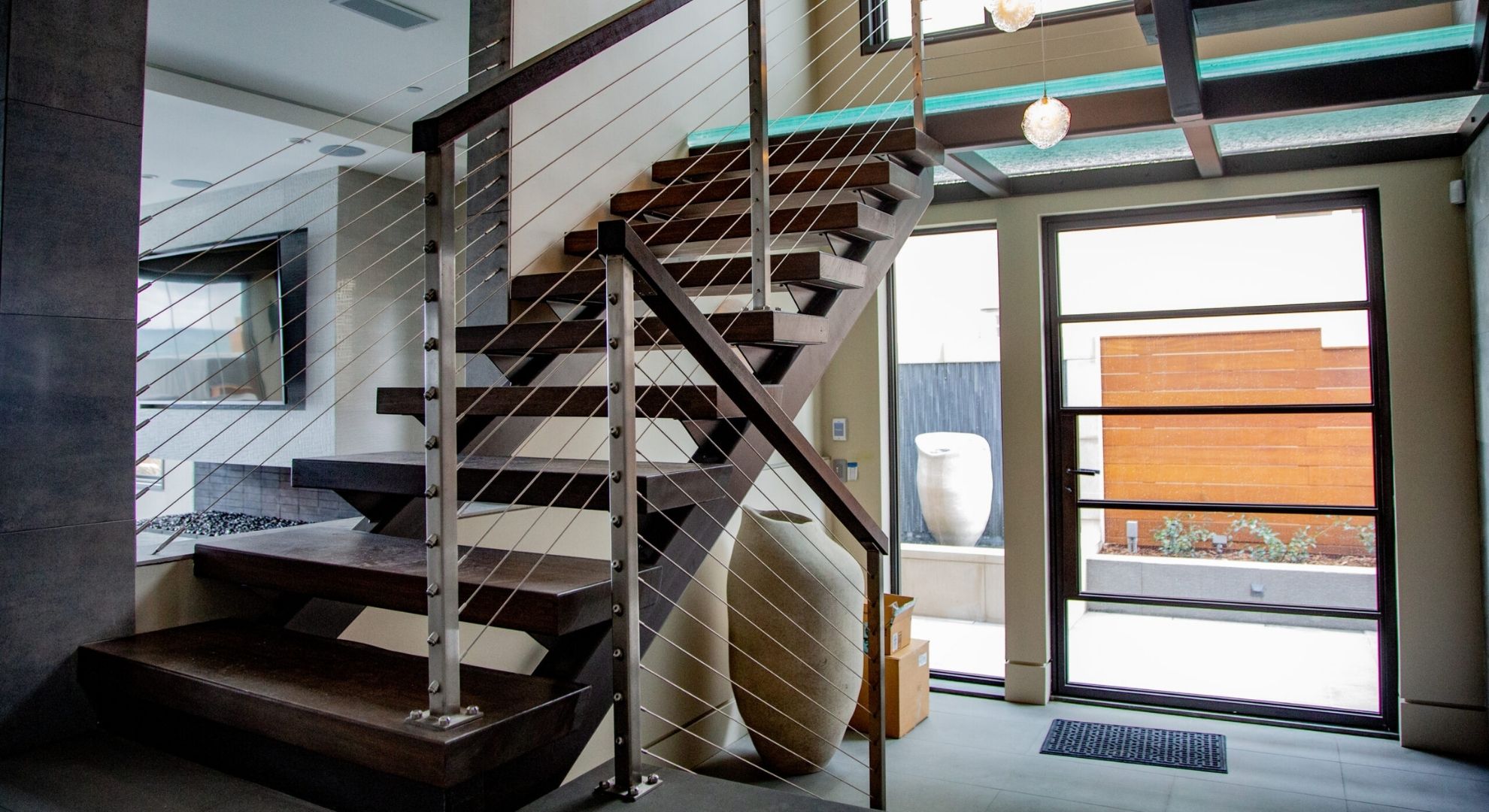Modern interior staircase with stainless steel cable railing and wood handrail in a bright, open-concept luxury home.