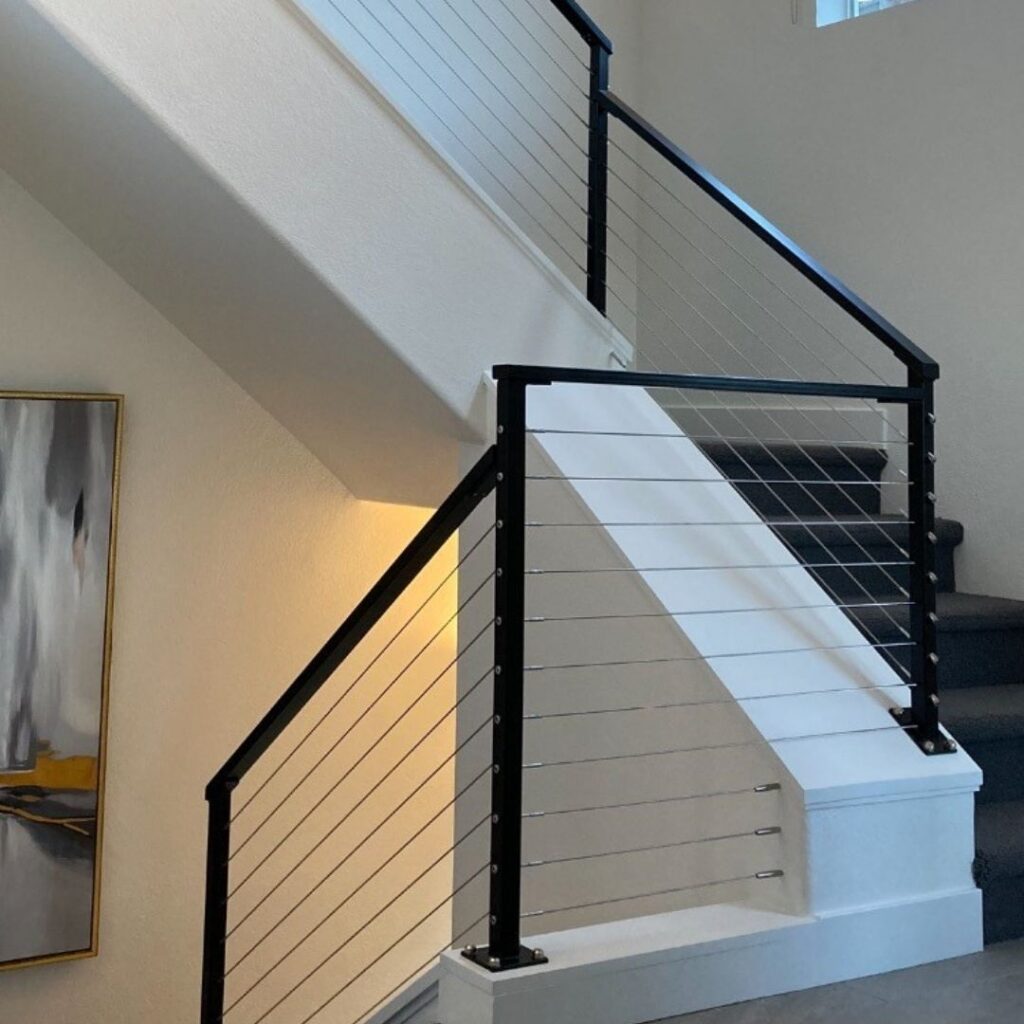 Minimalist staircase design featuring a mix of dark wood posts and horizontal stainless steel cables.