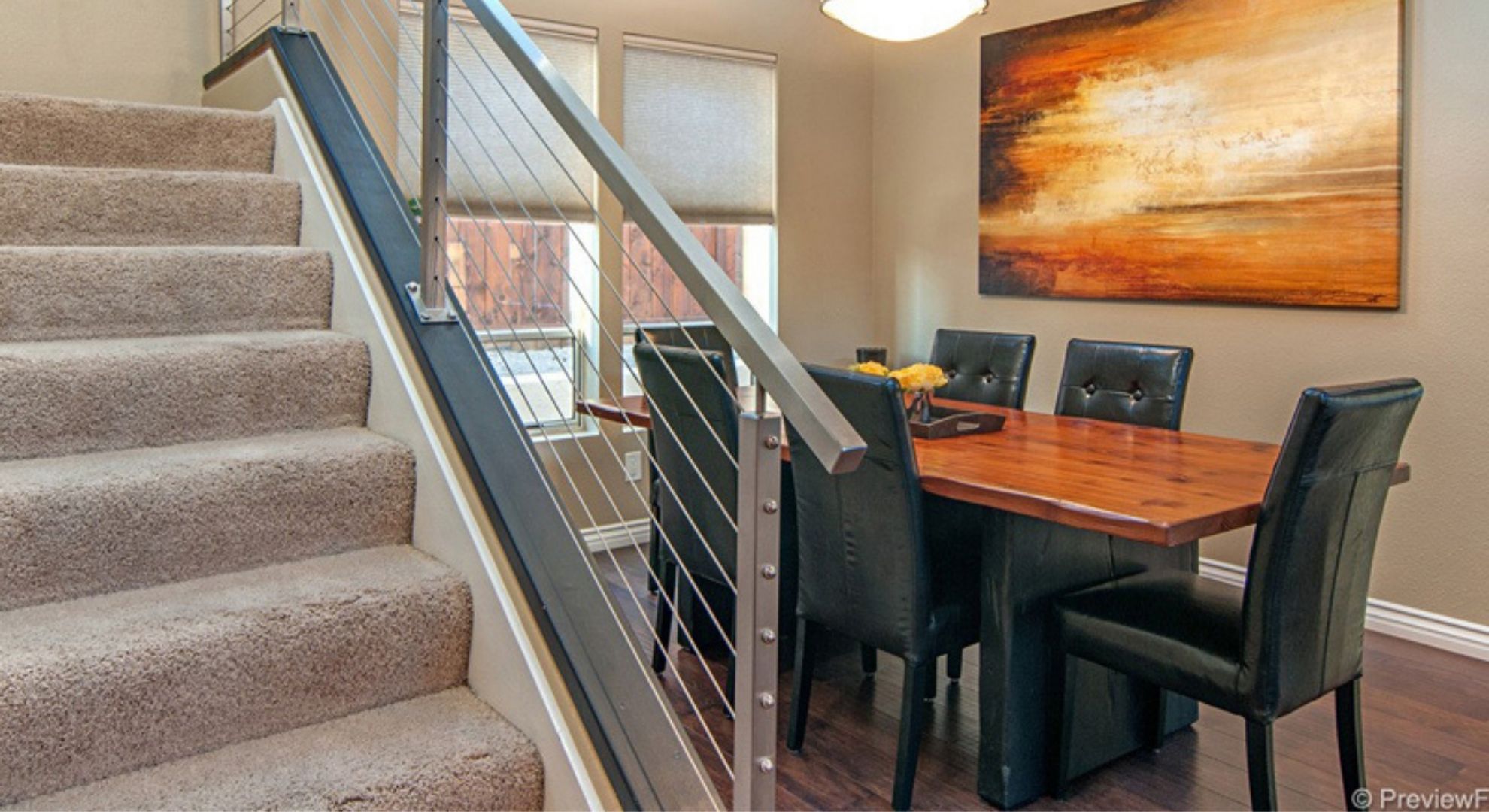 Modern luxury staircase featuring a stainless steel cable railing system with wooden handrails in a bright, sunlit home.
